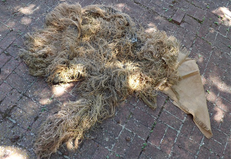 partially completed ghillie suit with burlap strings attached to netting.