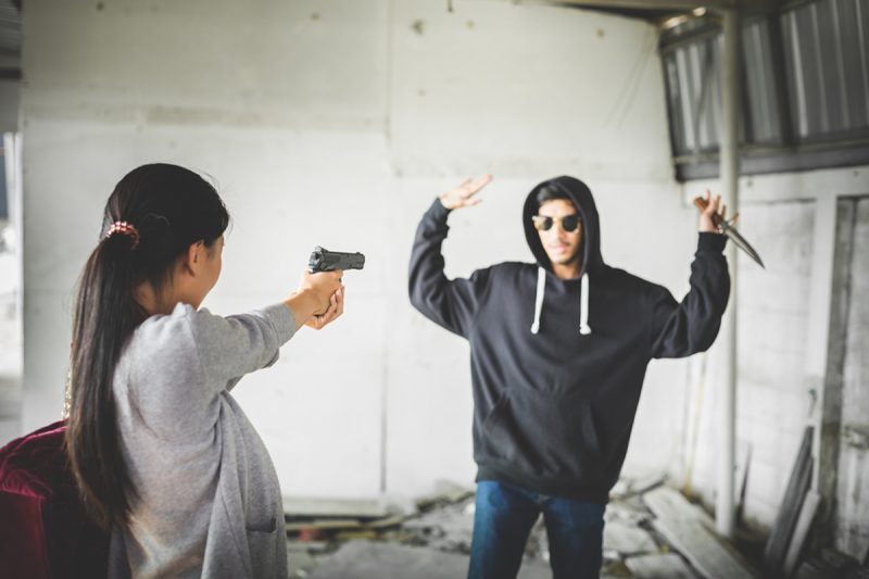 woman aiming handgun at assailant with a knife. Self-defense insurance featured image