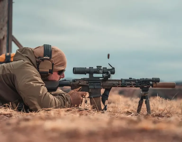 Man aiming a rifle on the ground.