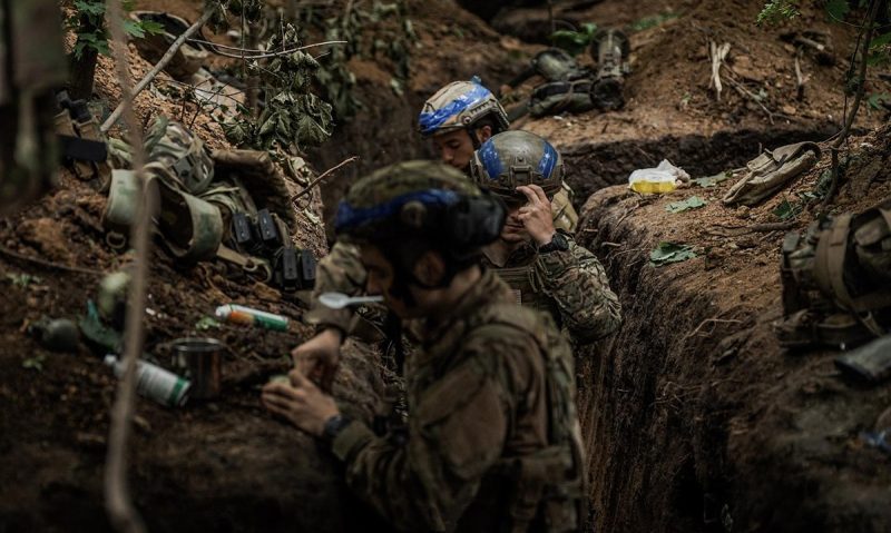 Ukrainian soldiers of the Azov Brigade grab something to eat in captured Russian trenches somewhere in the Ukraine kill zone.